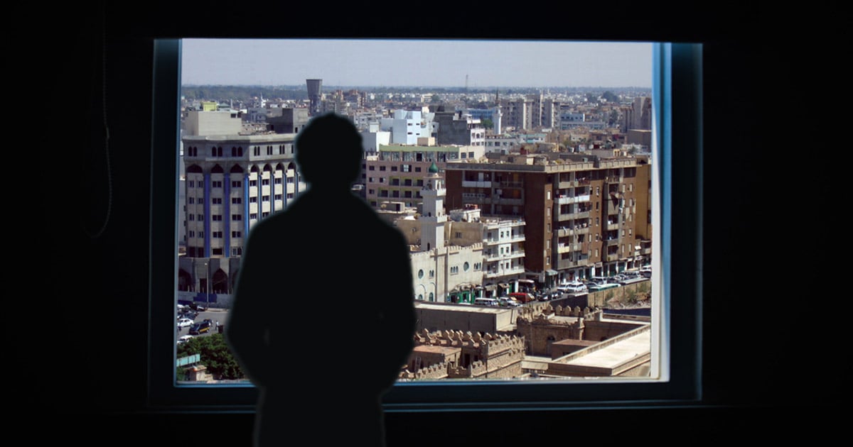 Sillhouette of a man looking through a window at a city