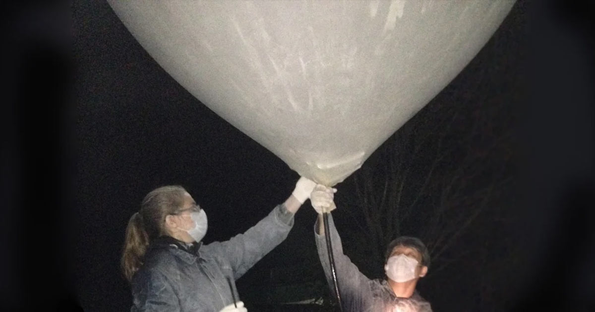 Two people are filling a very large balloon