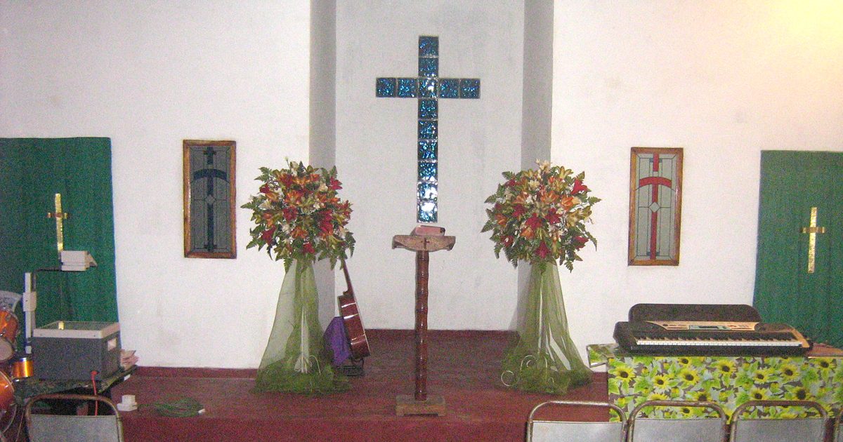 The inside of a church building shows crosses at the back of the stage, two flower arrangements and chairs arranged, ready for a gathering.