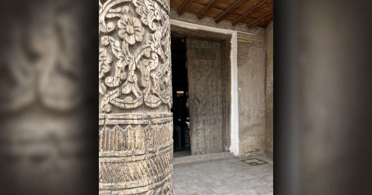 Entry to a building; a pillar with intricate carvings is in the foreground.