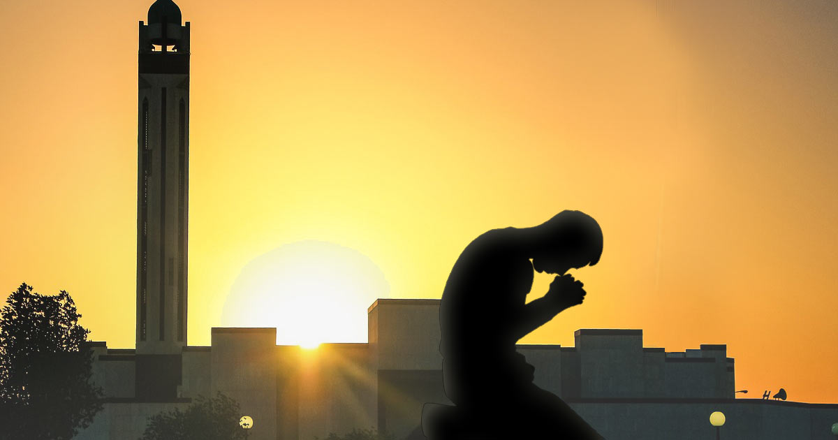 Man praying with mosque in the background